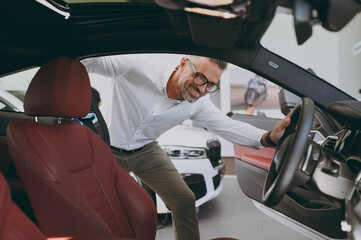Adult man customer buyer client wears shirt look inside get into car check interior think choose auto want to buy new automobile in showroom vehicle salon dealership store motor show. Sales concept.